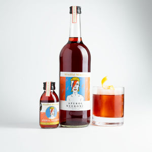 The small Aperol Negroni bottle is in the picture, alongside a large 750ml bottle. It is the same shape and similar label, but the bottle is a lot larger. Next to it is a glass of Aperol Negroni. It is a deep orange colour and is in a short tumbler glass with a large ice cube, and a lemon twist sitting on top of the ice cube. The background is white. 